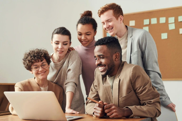 Eine Gruppe von fünf Menschen, die lächeln in einen Laptop schauen.